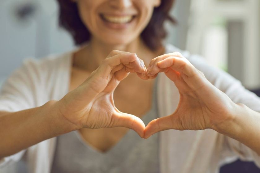A smiling woman making a heart shape with her hands.
