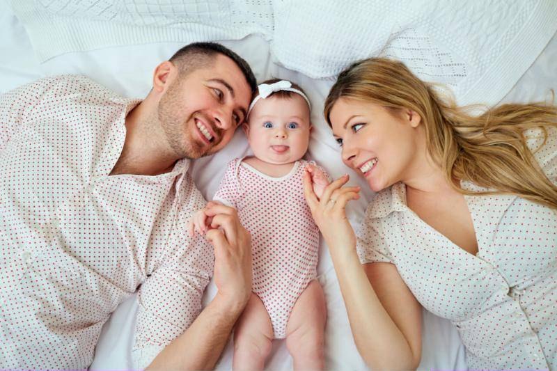 Two parents lying beside their smiling baby.