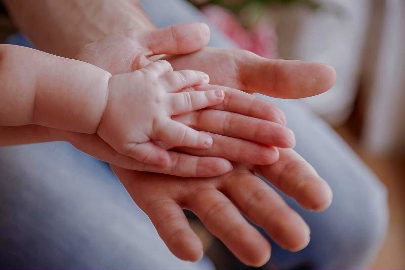 A baby's hand resting on an adult's open hand.