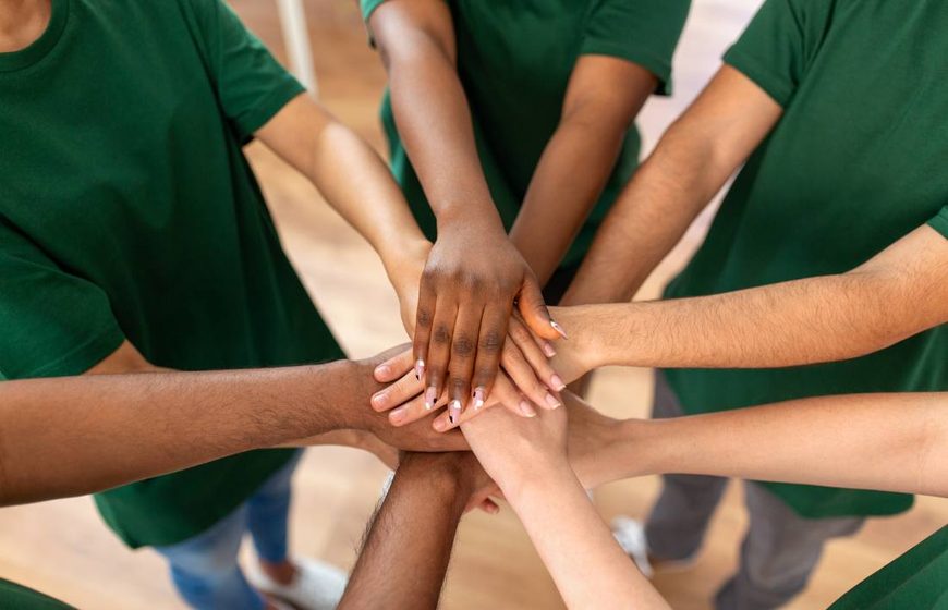 People in green T-shirts stacking their hands together in a circle.